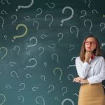 Serious business woman in front of question marks drawn on blackboard
