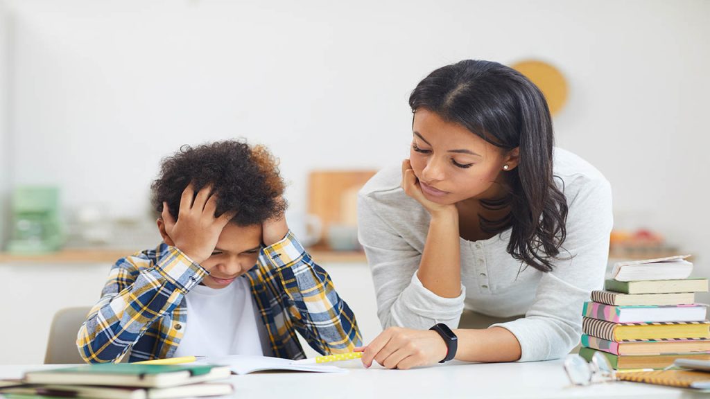 Portrait of teenage African boy studying at home and struggling with mother helping him, copy space