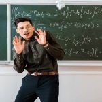 crumpled paper balls flying at frightened male teacher in classroom with chalkboard on background