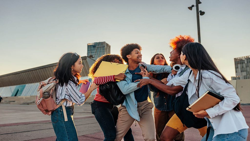 Two young classmates are engaged in a physical fight after school, they are pulling at each other while their female classmates are trying to calm them down.