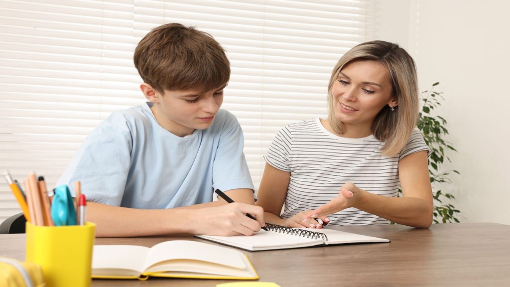 Smiling mother helping her son with homework at table indoors