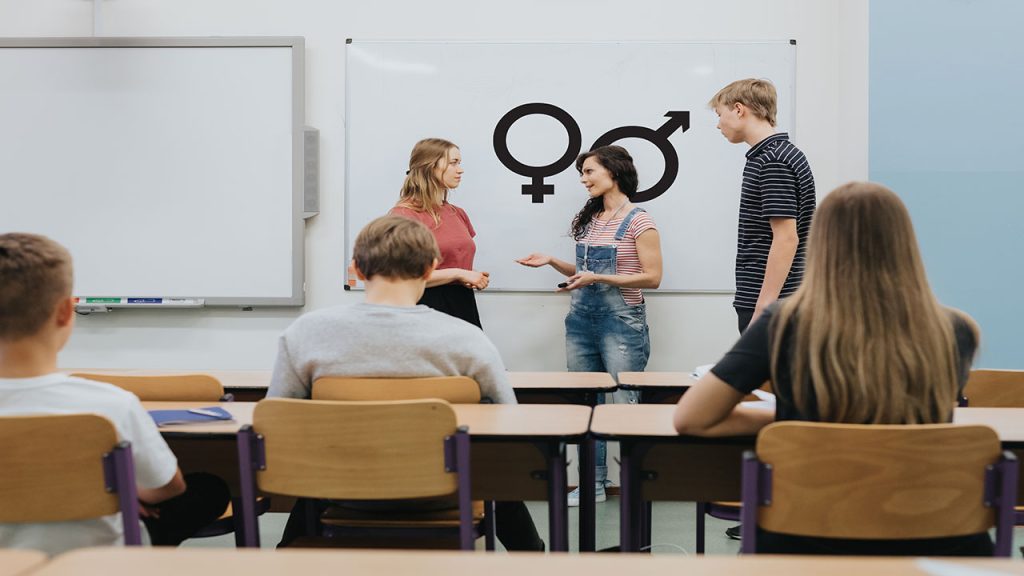 Young teacher is standing in front of the blackboard during sex education lesson