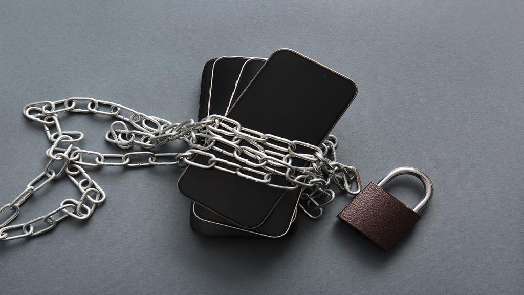 Different mobile phones with chain and padlock on dark background